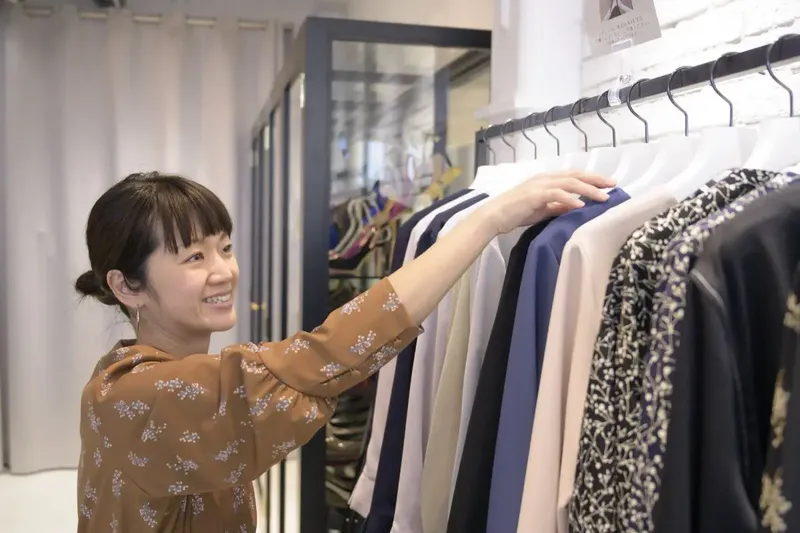 衣服のハンガーラックから洋服を選ぶ女性。在庫から商品を探して取り出す場面