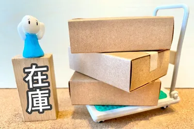 「在庫」と書かれた木製キューブと青いハンドル付き配送カート。在庫管理・配送の概念。