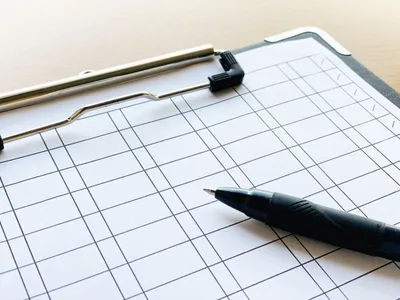 クリップボード上の方眼紙にペンを置き、手書きで在庫データを記録している様子