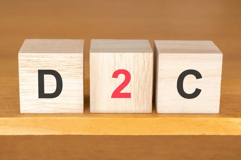 木製キューブに「D2C」と表記。ダイレクト・トゥ・コンシューマー（消費者直取引）の概念表現。