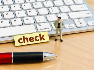 キーボード上のミニチュア人物と黄色い「check」の付箋。商品確認・品質チェック業務。