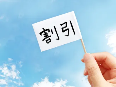 青空を背景に手が持ち上げた白い旗に「割引」と書かれた、セール・割引キャンペーンを象徴するイメージ