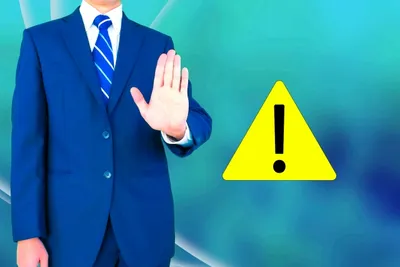 スーツのビジネスマンが左手で警告サインを示す。注意喚起と警戒を表現