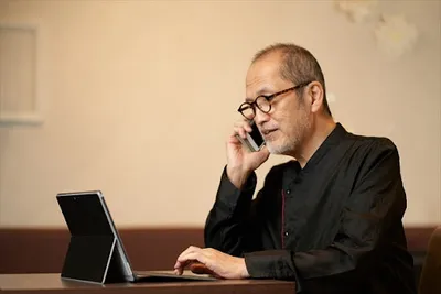 タブレットを持ちながら電話対応する中年男性。受注・顧客対応のシーン