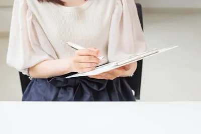 ピンクシャツの女性がデスクで注文フォームをペンで記入している