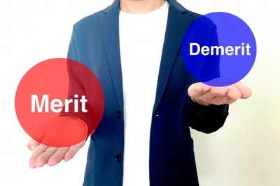 ビジネスマンが赤い「Merit」と青い「Demerit」のふきだしを両手に持つ比較イメージ