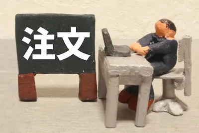黒板に『注文』と書き椅子に座る人形で顧客対応・受注受付・注文管理を表現