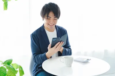 観葉植物のあるデスクでノートパソコンとスマートフォンを操作し、商品データを確認するせどり業務シーン