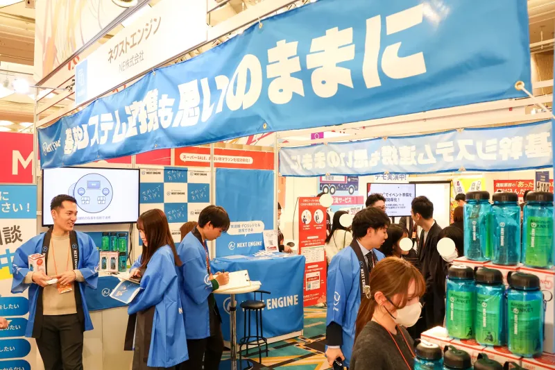 楽天新春カンファレンス2026の会場で、「基幹システム連携も思いのままに」という青い横断幕を掲げたネクストエンジンブースの全景。
